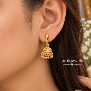 Könnte beinhalten: Ein goldener Creolen-Ohrring mit einem glockenförmigen Jhumka-Anhänger, der filigrane Gitterdetails und kleine hängende Perlen am unteren Rand aufweist. Der Text anikjewels mit einem Herzsymbol ist in der unteren rechten Ecke zu sehen.