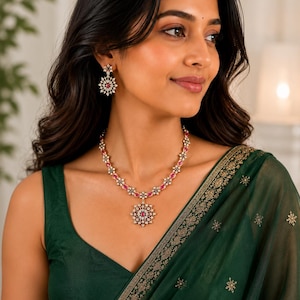 May include: A gold-toned necklace and matching drop earrings set featuring small oval-shaped pink stones and clear white crystals arranged in a floral pattern. The necklace includes a central circular pendant with a matching floral design.