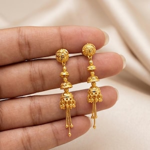 May include: A pair of gold drop earrings featuring a stud top with a textured spherical design, followed by two smaller tiered bell-shaped components, and a larger bell-shaped base with dangling beaded chains extending from the bottom edge.