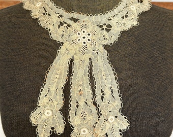 May include: A delicate ivory lace collar with a scalloped edge and a central bow. The lace features small, round beads throughout.