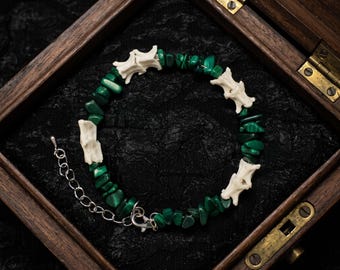 May include: A bracelet featuring alternating segments of small, irregular, deep green malachite stone chips and off-white, textured bone-like vertebrae pieces. The bracelet includes a silver-toned metal chain extender and a lobster claw clasp.