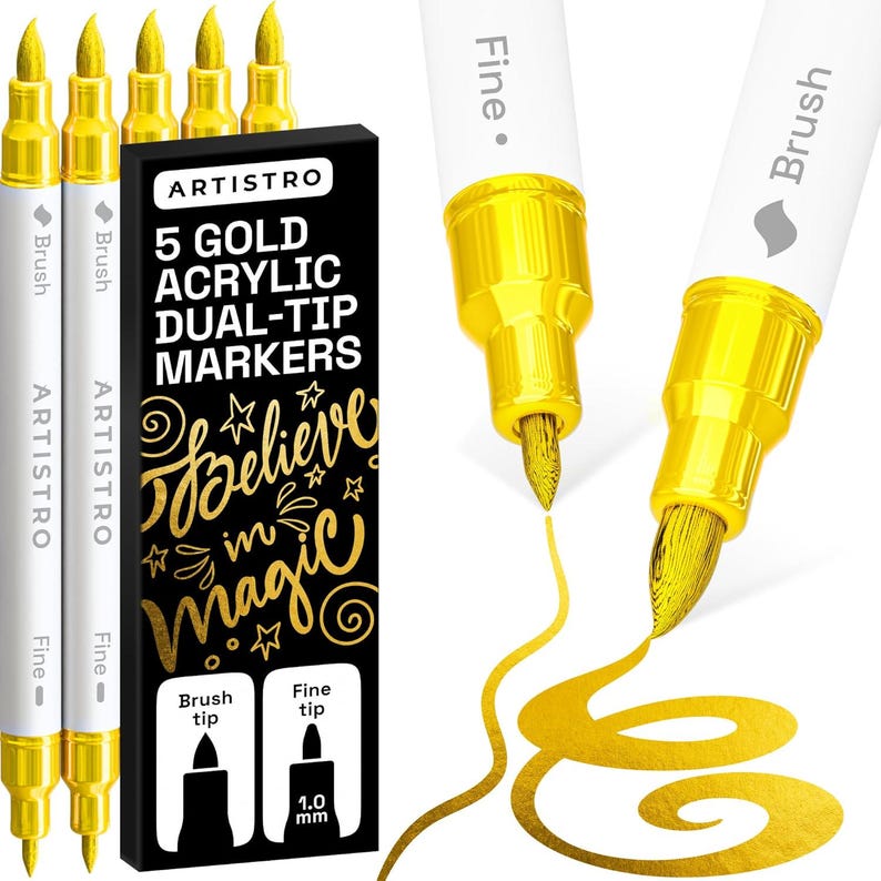 May include: Five gold acrylic dual-tip markers with white barrels and gold caps. The black packaging box displays the text 5 GOLD ACRYLIC DUAL-TIP MARKERS and Believe in magic. Two markers are shown with exposed fine and brush tips drawing gold lines.