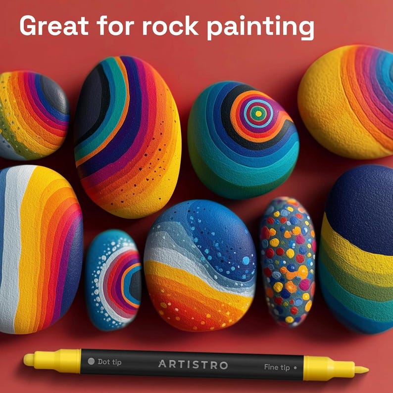 May include: A selection of brightly painted rocks in shades of blue, yellow, orange, and purple. The rocks feature abstract designs and patterns. The text "Great for rock painting" is at the top, and a yellow and black ARTISTRO marker is at the bottom.