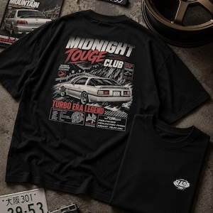 May include: A black t-shirt featuring a large graphic on the back with a white sports car, the text MIDNIGHT TOUGE CLUB, and TURBO ERA LEGEND. A smaller black t-shirt is folded nearby with a small white logo on the chest that reads GLAZED.