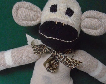 Puede incluir: Un mono de calcetín blanco y negro con una pajarita de estampado de leopardo marrón y negro. El mono lleva pantalones blancos con manchas negras.