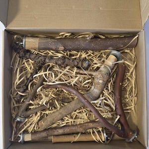 May include: A cardboard box filled with shredded paper packing material containing several natural wooden branches and sticks. Each piece of wood features metal hardware attachments at the ends, including washers and wing nuts for secure mounting.