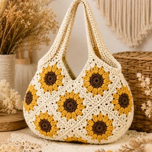 May include: A cream-colored crochet handbag featuring a repeating pattern of sunflower motifs. Each sunflower has a dark brown center surrounded by bright yellow petals, all connected by cream yarn. The bag has two integrated handles.