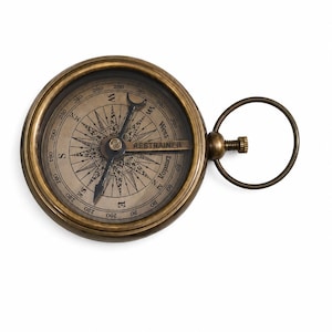 Puede incluir: Una brújula redonda de latón de estilo antiguo con una esfera metálica que muestra una rosa de los vientos detallada, puntos cardinales y marcas de grados. La palabra RESTRAINER está impresa en el centro. Un anillo metálico está unido al lado.