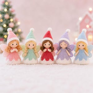 May include: Five needle-felted fairy figurines arranged in a row. Each figure wears a pointed hat with a white pom-pom, a dress with a white hem, and has small wings. The fairies feature different hair colors and dress colors: pink, mint, red, purple, and blue.