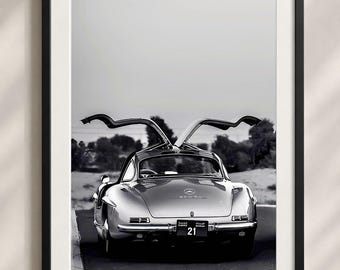 Könnte beinhalten: Ein schwarz-weiß gerahmter Druck, der die Rückansicht eines klassischen Mercedes-Benz 300SL mit geöffneten Flügeltüren zeigt. Das Auto trägt ein Nummernschild mit der Nummer 21 und dem Text CLASSIC SHARJAH vor einer Wüstenlandschaft.