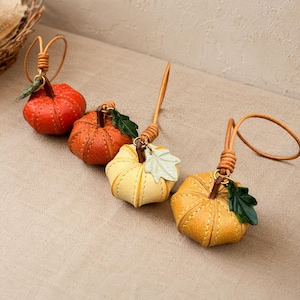 Puede incluir: Cuatro adornos hechos a mano con forma de calabaza en cuero texturizado en tonos rojo, naranja, amarillo y dorado. Cada calabaza presenta costuras visibles, un peque&ntilde;o lazo de cuero para colgar y un detalle de hoja verde unido al tallo.
