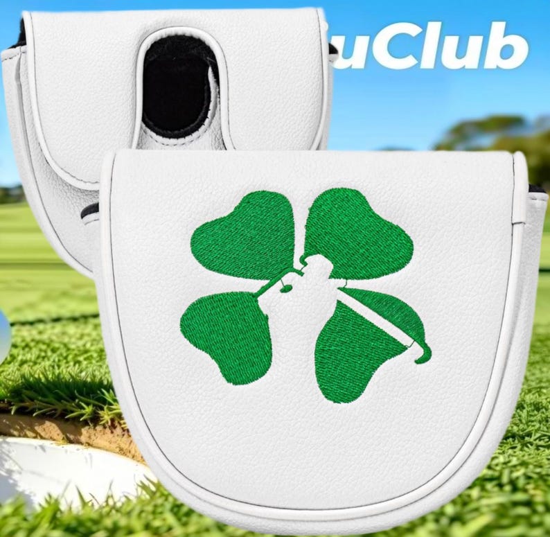 Op de afbeelding: Een witte mallet putter headcover met een geborduurd groen klavertjevier-ontwerp waarin een golfclub-afbeelding in het midden is verwerkt. De hoes heeft een gestructureerde, ronde vorm met witte biezen langs de randen en een zwarte binnenkant.