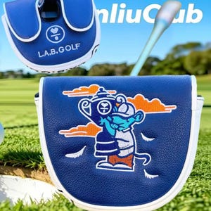 May include: A blue and white golf putter headcover featuring the text L.A.B.GOLF and an embroidered graphic of a cartoon character holding a trophy. The design includes orange clouds and white feathers on a textured blue surface with white trim.