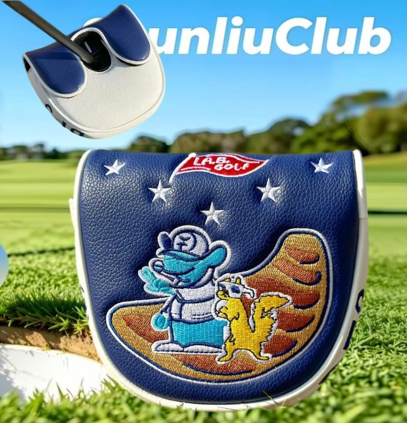 May include: A navy blue and white golf putter headcover featuring an embroidered graphic of a blue character and a yellow squirrel on a brown crescent shape, with white stars and a red L.A.B. GOLF flag logo stitched on the textured synthetic leather.