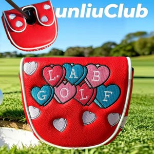 Op de afbeelding: Een rode golfputter-headcover met witte biezen en geborduurde hartjes in roze, blauw en wit. De hartjes tonen de letters L, A, B, G, O, L, F in wit stiksel. De hoes heeft een gestructureerd oppervlak en een magnetische sluiting.
