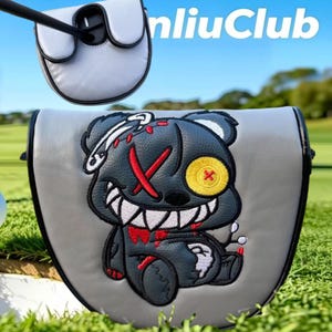 May include: A grey golf putter headcover featuring an embroidered dark grey bear with a yellow button eye, a red stitched X eye, and sharp white teeth. The design includes red accents and a safety pin detail. The text nliuClub is visible above.