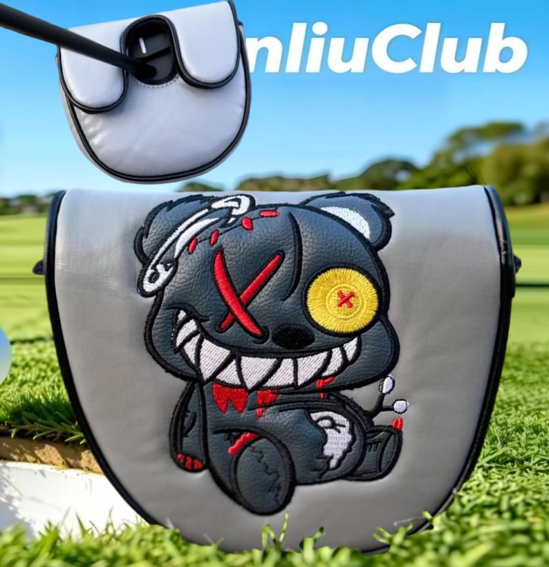 May include: A grey golf putter headcover featuring an embroidered dark grey bear with a yellow button eye, a red stitched X eye, and sharp white teeth. The design includes red accents and a safety pin detail. The text nliuClub is visible above.