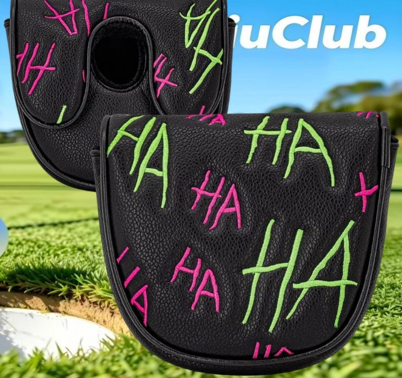 May include: A black putter headcover featuring a textured surface with embroidered "HA" text in bright neon green and hot pink. The design includes multiple repetitions of the word "HA" scattered across the front and top of the protective cover.