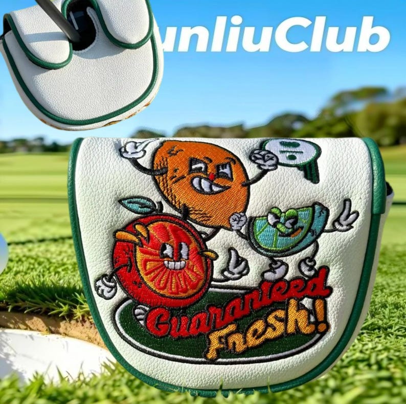 May include: A white golf putter headcover with green trim featuring embroidered cartoon fruit characters including an orange, a lime, and a brown fruit. The text "Guaranteed Fresh!" is embroidered in red and yellow below the fruit characters.