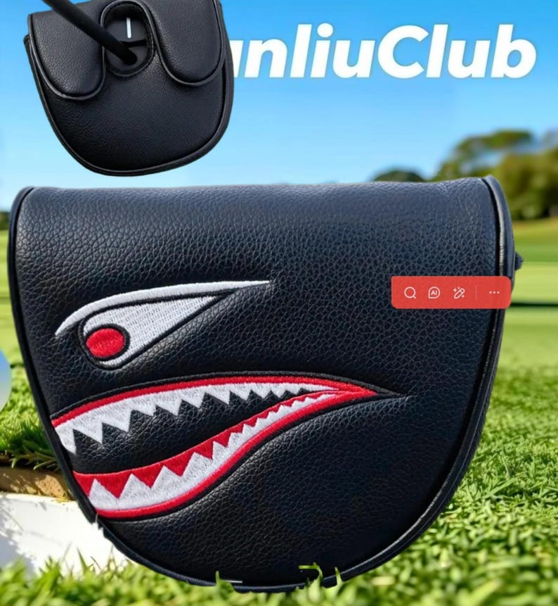 May include: A black mallet putter headcover featuring a textured leather-like finish and an embroidered shark mouth graphic with white teeth and red accents. The design includes a stylized eye with a red pupil. The text "nliuClub" is visible.