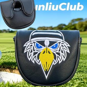 May include: A black leather-like golf putter headcover featuring an embroidered eagle head graphic with blue eyes and a yellow beak. The design includes white outlines and a white cap detail. The text "unliuClub" is visible in the upper right corner.