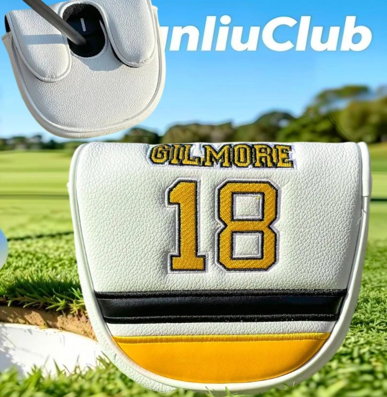 May include: A white golf putter headcover featuring the name GILMORE and the number 18 embroidered in yellow with black outlines. The cover includes a horizontal black stripe and a yellow band at the bottom, with a textured faux leather finish.