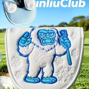 May include: A white golf putter headcover featuring an embroidered yeti character in blue and white tones, holding a staff. The cover is decorated with stitched snowflake patterns and includes a smaller view of the top with the text unliuClub.