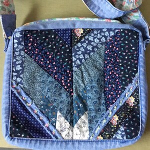 May include: A patchwork crossbody bag with a denim exterior and a floral-patterned strap. The bag features a quilted design with various shades of blue and floral fabrics. The strap is approximately 100 cm long.