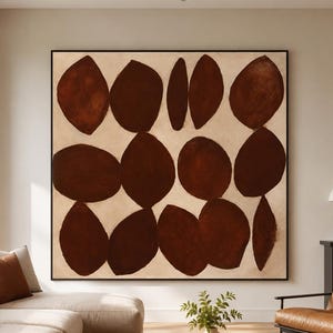 Puede incluir: Una gran pieza de arte mural cuadrada que presenta una cuadrícula de formas orgánicas de color marrón oscuro, similares a hojas, pintadas sobre un fondo beige claro. La obra está enmarcada con un borde negro fino sobre una pared neutra.