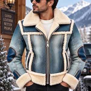Könnte beinhalten: Eine blau-weiße Lederjacke in Distressed-Optik mit einem dicken, cremefarbenen Lammfellkragen, Ärmelbündchen und Saum. Die Jacke verfügt über einen silbernen Reißverschluss, dunkelblaue Leder-Ellbogenpatches und dunkelblaue Ledernähte.