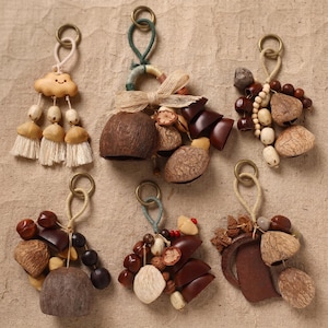 May include: Six decorative hanging ornaments featuring natural elements. One includes a wooden cloud with tassels. Others feature clusters of dark brown seed pods, smooth wooden beads, textured nuts, and beige fabric bows, all suspended from metal rings.