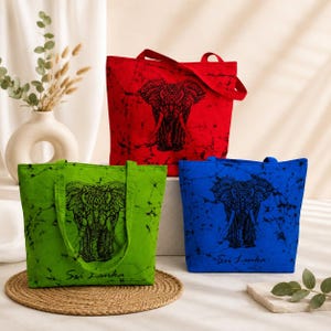 May include: Three rectangular tote bags in red, lime green, and royal blue, each featuring a black batik-style elephant graphic and the text Sri Lanka printed in black. The bags have matching fabric handles and a textured, mottled fabric finish.