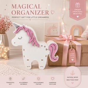 K&ouml;nnte beinhalten: Ein wei&szlig;er Holztisch-Organizer in Einhornform mit rosa M&auml;hne und Schweif sowie kleinen Sternausschnitten. Das Einhorn steht neben einem braunen Geschenkpaket, das mit einem rosa Band und einem Anh&auml;nger mit der Aufschrift MADE WITH LOVE versehen ist.