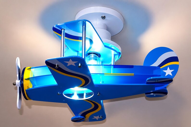 Peut inclure: Un plafonnier en forme d'avion bleu avec des accents blancs et jaunes. Le design comprend une h&eacute;lice blanche, une ampoule centrale et des &eacute;toiles blanches sur les ailes et la queue. Il est fix&eacute; sur une base circulaire blanche.