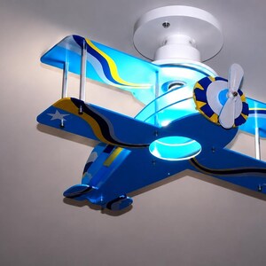 Peut inclure: Un plafonnier en forme de biplan bleu avec des accents jaunes et blancs. L'avion pr&eacute;sente une h&eacute;lice blanche, deux jeux d'ailes et des graphismes d'&eacute;toiles blanches sur le bout des ailes. Il est fix&eacute; au plafond par une base blanche.