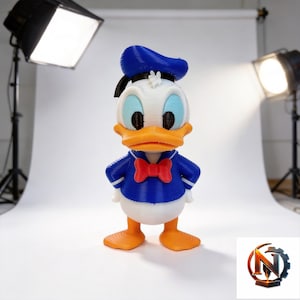 Op de afbeelding: Een 3D-geprint figuur van een witte eend met een blauwe matrozenmuts, een blauw shirt met witte randen, een rode vlinderdas en oranje voeten. Het figuur heeft een textuur die is ontstaan door het 3D-printproces en staat rechtop.