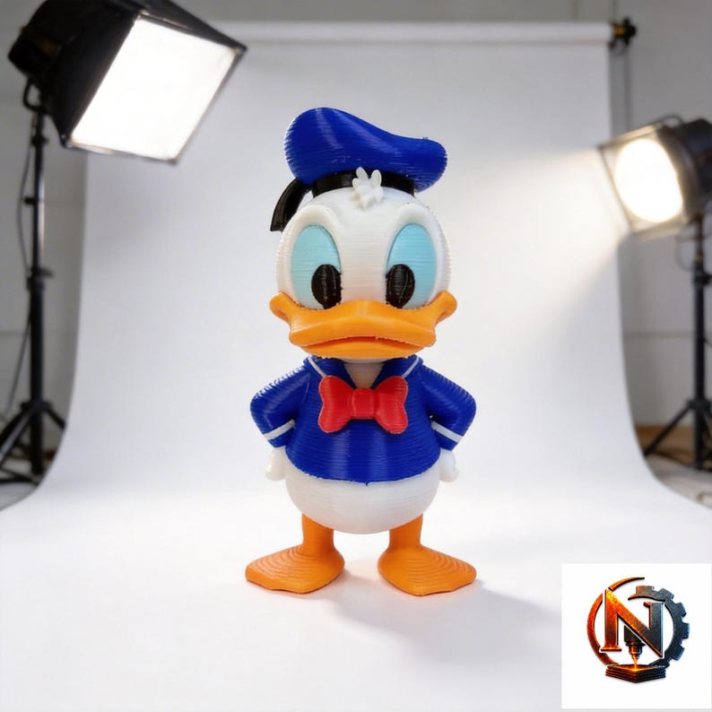 Op de afbeelding: Een 3D-geprint figuur van een witte eend met een blauwe matrozenmuts, een blauw shirt met witte randen, een rode vlinderdas en oranje voeten. Het figuur heeft een textuur die is ontstaan door het 3D-printproces en staat rechtop.