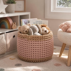 May include: A round, pink and tan crochet basket filled with stuffed animals and books. The basket contains a teddy bear, a bunny, and a lion. The books are titled "W" and "Guess How Much". The basket sits on a patterned rug.