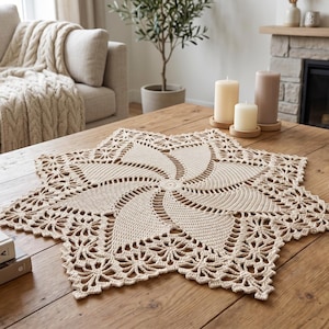 May include: A beige crochet doily featuring a central spiral pattern radiating outward into six pointed star-shaped sections with intricate openwork lace detailing along the edges, crafted from fine yarn in a circular and geometric design.