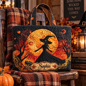 May include: A quilted tote bag featuring a black silhouette of a witch in a hat against a large orange moon, surrounded by dark trees and autumn leaves. The bag has a rectangular label at the bottom with the name Sophia printed in black script.