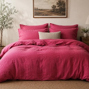 May include: A vibrant magenta bedding set consisting of a large duvet cover and four matching rectangular pillowcases, accompanied by a single smaller, rectangular beige accent pillow placed centrally in front of the magenta pillows.
