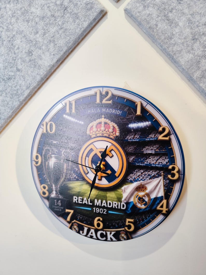 May include: A round wall clock featuring a Real Madrid theme with the club crest, a stadium background, the Champions League trophy, and a flag. The clock face displays the text Hala Madrid, Real Madrid 1902, and the name Jack with gold numbers.