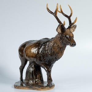 Könnte beinhalten: Eine dunkelbraune, glänzende Hirschfigur, die auf einem Sockel steht. Der Hirsch hat strukturiertes Fell, spitze Ohren und hellbraune Geweihe. Der Text "PANNA MAKES CREATURES" und ein kleines Logo sind oben links im Bild zu sehen.