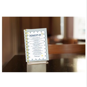 May include: A printed "Homestay" sign with a white background, blue and white striped border, and yellow accents. The sign is displayed on a clear acrylic stand. The text includes check-in/out details, cleaning, and other policies.