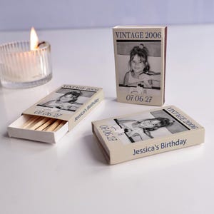 May include: Three rectangular matchboxes with beige covers featuring a black and white photograph of a child, the text VINTAGE 2006, 07.06.27, and Jessica's Birthday. One box is open, revealing wooden matches inside, while two are closed.