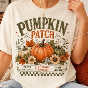 May include: An off-white short-sleeve t-shirt featuring a graphic print with the text PUMPKIN PATCH, FRESH FROM THE PATCH, AUTUMN HARVEST, and FARM GROWN. The design includes illustrations of orange, green, and white pumpkins, sunflowers, and leaves.