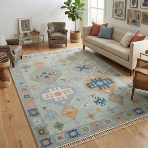May include: A large, rectangular area rug with a light blue background and a geometric pattern in shades of orange, blue, and beige. The rug has a fringed edge and is placed in a living room setting.