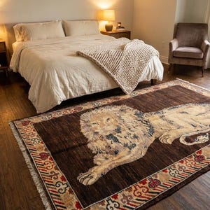 Puede incluir: Una alfombra rectangular que presenta una gran ilustración central de un león en tonos crema y bronceado sobre un fondo marrón oscuro, enmarcada por un borde decorativo con patrones geométricos rojos, blancos y negros y flecos blancos.