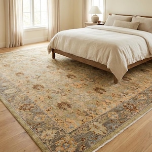 May include: A large rectangular area rug featuring a complex floral pattern in muted shades of sage green, beige, and brown. The rug has a wide, dark border with intricate botanical motifs and a lighter, distressed-look center field.