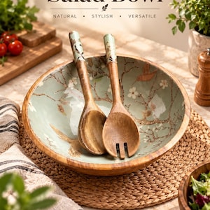 May include: A round wooden salad bowl and a pair of matching serving utensils. The interior of the bowl and the handles of the utensils feature a light green finish with a painted design of brown branches, white flowers, and a bird. Text reads Salad Bowl.